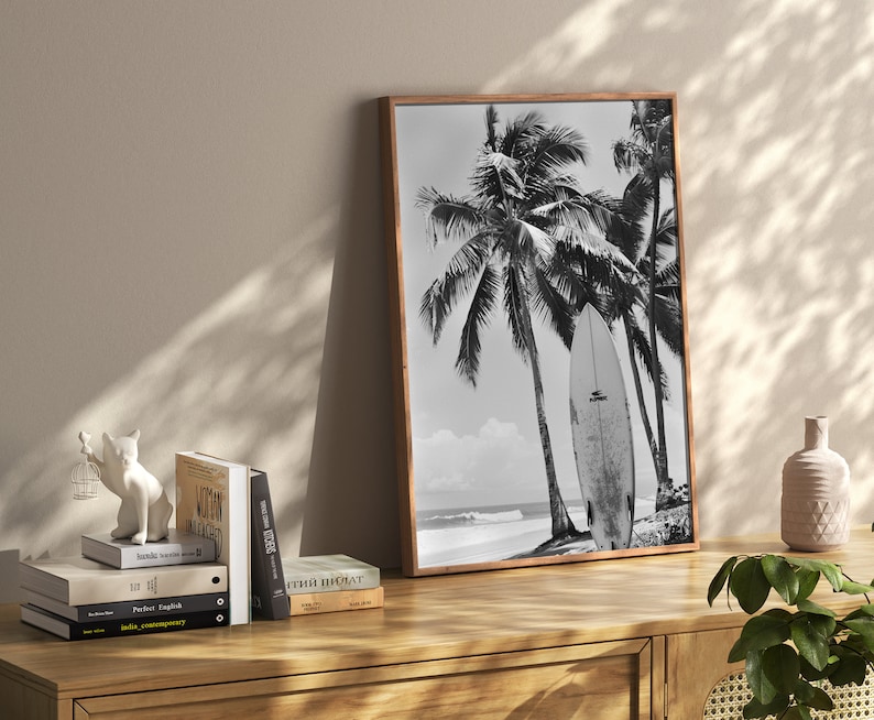 May include: Black and white photograph of palm trees and a surfboard on a beach. The image is framed in a wooden frame.