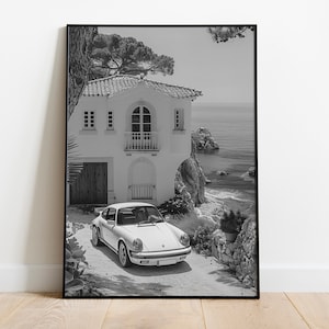 K&ouml;nnte beinhalten: Ein Schwarzwei&szlig;foto eines wei&szlig;en Porsche 911, der vor einem wei&szlig;en Haus mit Blick auf das Meer geparkt ist.