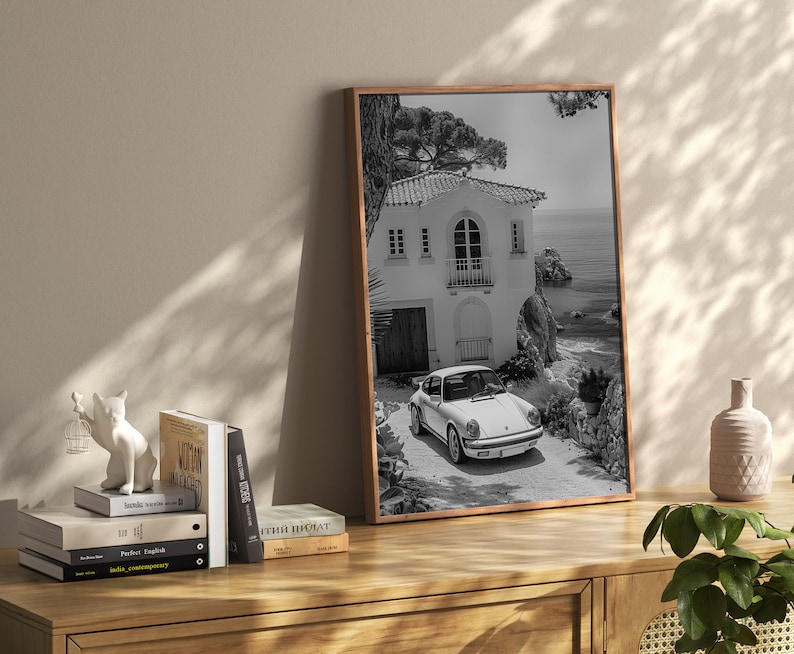 K&ouml;nnte beinhalten: Schwarzwei&szlig;foto eines wei&szlig;en Oldtimers, der vor einem wei&szlig;en Haus mit einem Steinbogen geparkt ist. Das Haus befindet sich auf einer Klippe mit Blick auf das Meer.
