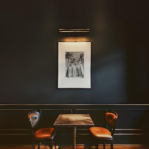 May include: A black and white photograph of palm trees and surfboards hangs on a dark wall above a wooden table with two brown leather chairs. The table has a dark wood top and a metal base.