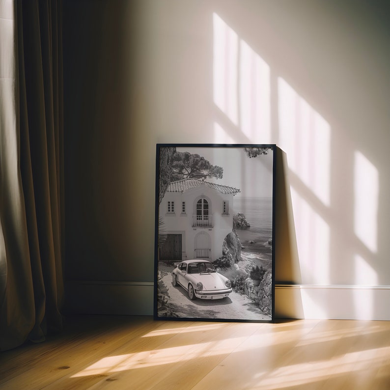 K&ouml;nnte beinhalten: Ein Schwarzwei&szlig;foto eines wei&szlig;en Autos, das vor einem wei&szlig;en Haus mit rotem Ziegeldach geparkt ist. Das Haus ist von B&auml;umen und B&uuml;schen umgeben. Das Auto ist ein klassischer Porsche 911.
