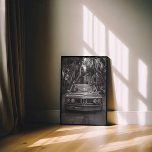 Puede incluir: Fotograf&iacute;a en blanco y negro de un coche cl&aacute;sico conduciendo por una calle bordeada de &aacute;rboles. El coche es un BMW vintage con una parrilla cromada y faros redondos. La foto est&aacute; enmarcada en un marco negro.