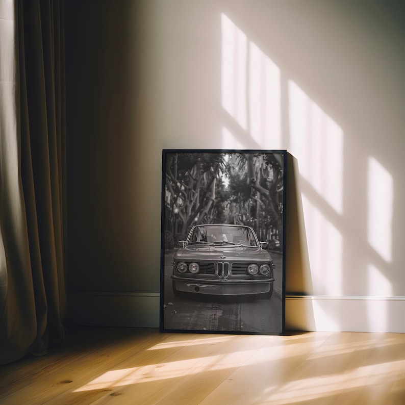 Puede incluir: Fotograf&iacute;a en blanco y negro de un coche cl&aacute;sico conduciendo por una calle bordeada de &aacute;rboles. El coche es un BMW vintage con una parrilla cromada y faros redondos. La foto est&aacute; enmarcada en un marco negro.
