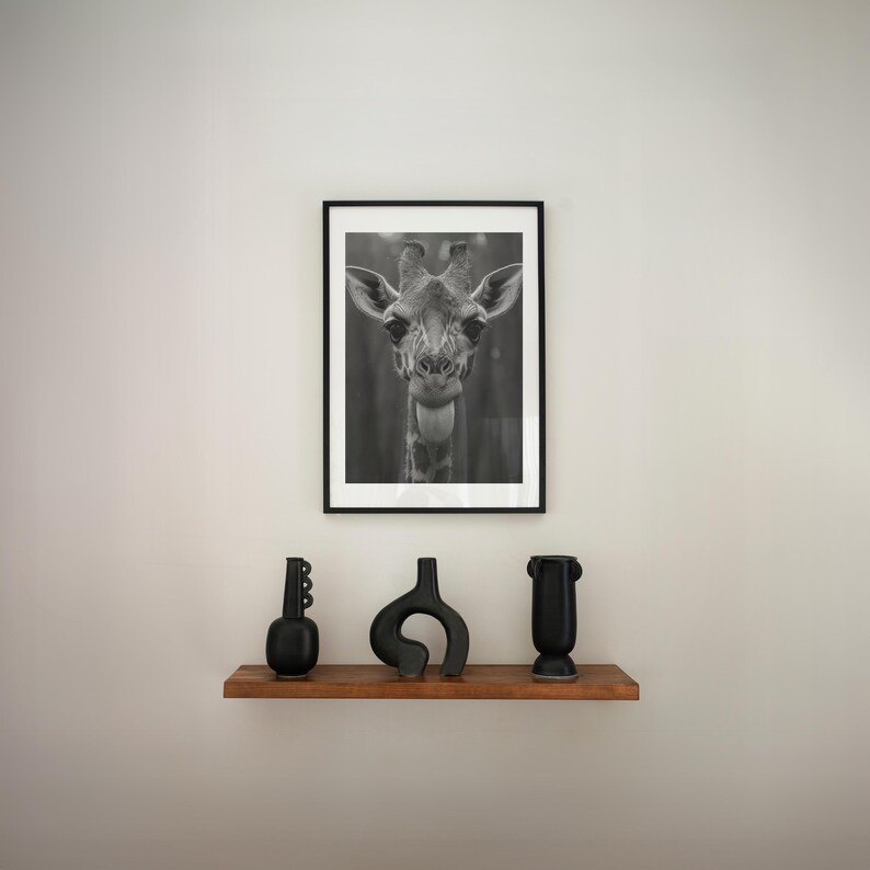 May include: A black and white photograph of a giraffe's head in a black frame hangs above a wooden shelf with three black ceramic vases.