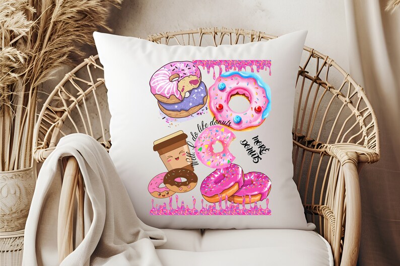 May include: White throw pillow with a colorful donut design. The design includes various donuts with pink, purple, and blue frosting, sprinkles, and the text "We like donuts" and "More donuts".