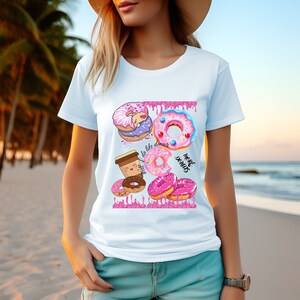 May include: Light blue t-shirt featuring a colorful donut graphic. The design includes various donuts with pink frosting, sprinkles, and the text "I do like donuts" and "More donuts". The shirt is made of a soft material.