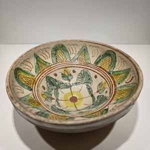 Può includere: Una ciotola in ceramica dipinta a mano con un motivo floreale. La ciotola presenta una base color crema con motivi floreali verdi, gialli e marroni. Il bordo è di colore marrone chiaro. La ciotola è probabilmente vintage o antica.