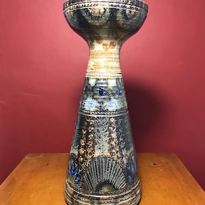 Peut inclure: Un vase en céramique brun et bleu, haut et évasé, avec un fond étroit. Le vase est décoré de motifs et de dessins complexes.