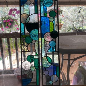 May include: Two stained glass panels with a geometric design featuring circles in shades of blue, green, and white.