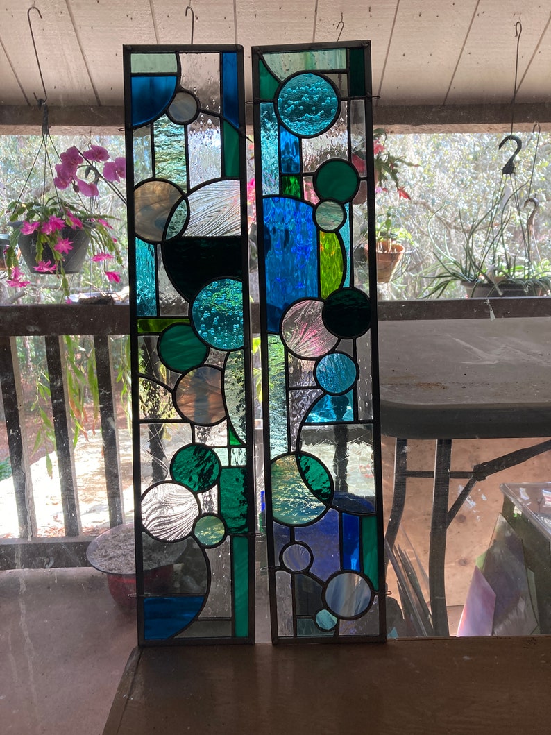 May include: Two stained glass panels with a geometric design featuring circles in shades of blue, green, and white.