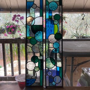 May include: Two stained glass panels with a geometric design featuring circles in shades of blue, green, and white.