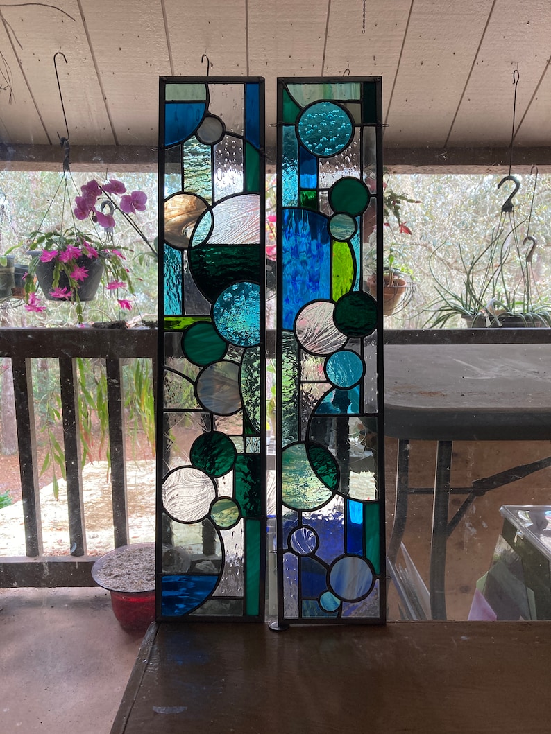 May include: Two stained glass panels with a geometric design featuring circles in shades of blue, green, and white.