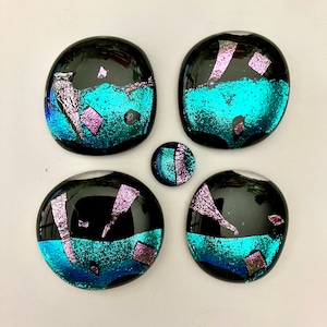 May include: Five glass paperweights with a black background and iridescent blue and pink accents. The paperweights are round and have a slightly uneven surface.