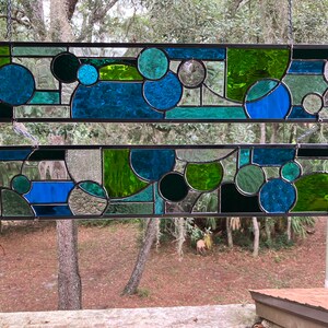 May include: Two stained glass panels with a geometric design featuring circles and abstract shapes in shades of blue and green.