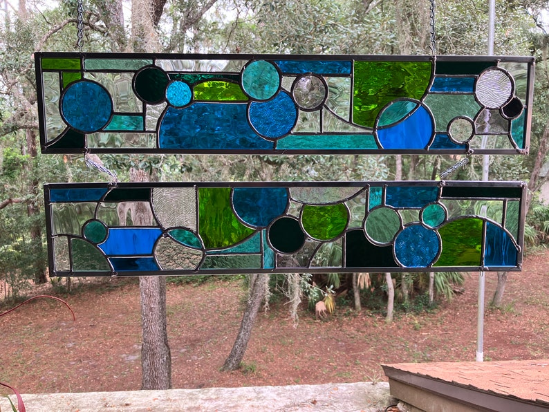 May include: Two stained glass panels with a geometric design featuring circles and abstract shapes in shades of blue and green.