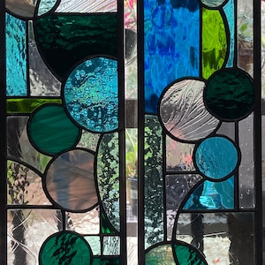 May include: Two stained glass panels with a geometric design featuring circles and squares in shades of blue, green, and white.