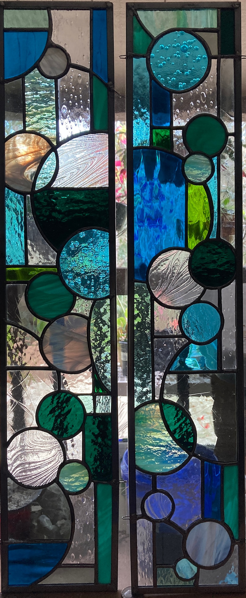 May include: Two stained glass panels with a geometric design featuring circles and squares in shades of blue, green, and white.