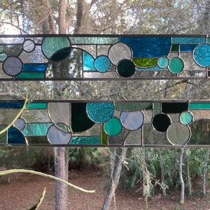 May include: Two stained glass panels with a geometric design featuring circles and squares in shades of blue, green, and grey.