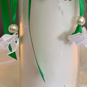 May include: A clear glass jar with a white lid, decorated with green ribbon and white bows. The jar is filled with a white substance, possibly a candle.