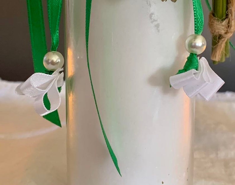 May include: A clear glass jar with a white lid, decorated with green ribbon and white bows. The jar is filled with a white substance, possibly a candle.