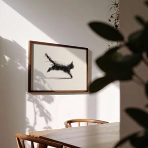 May include: A framed artwork featuring a black cat in motion, depicted with a blurred effect, creating a sense of speed. The artwork is set against a white background, framed in a dark wood. The piece is mounted on a white wall.