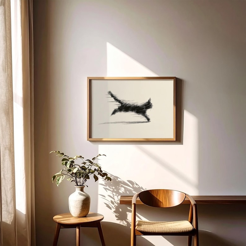 May include: A framed artwork featuring a black cat in motion, rendered with a blurred effect, suggesting speed. The artwork is set against a cream-colored background within a gold-toned frame. The image is displayed on a neutral-colored wall.