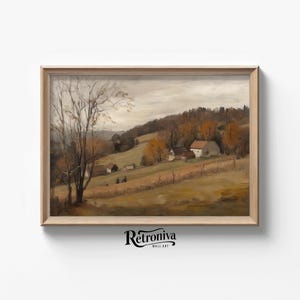 May include: A framed landscape painting depicts a rural scene with rolling hills, trees, and small buildings. The artwork features a muted color palette of browns, greens, and yellows, with a cloudy sky. The painting is in a light-colored wooden frame.