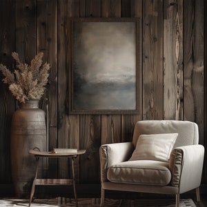 The painting of abstract art is displayed in a dark wooden frame with a earthy abstract art. There is an armchair in the room, a flower in a vase and a book on the table.