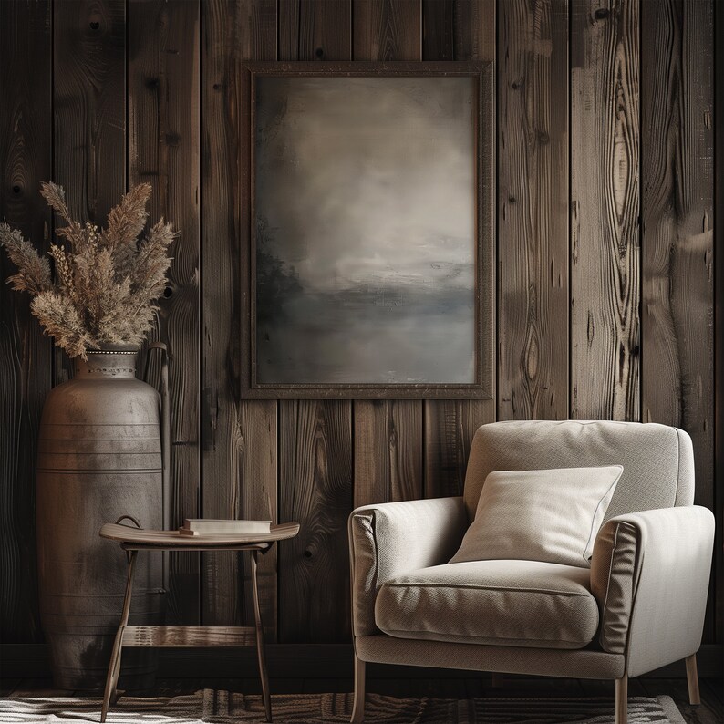 The painting of abstract art is displayed in a dark wooden frame with a earthy abstract art. There is an armchair in the room, a flower in a vase and a book on the table.