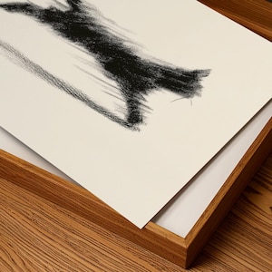 May include: Abstract charcoal drawing on white paper, featuring a bold, textured black stroke. The artwork is presented in a natural wood frame, creating a contrast between the dark art and the light background.