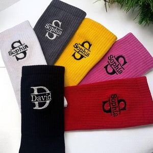 Op de afbeelding: Vijf paar sokken met geborduurde namen. De sokken zijn in verschillende kleuren, waaronder zwart, grijs, geel, roze en rood. De namen die op de sokken zijn geborduurd zijn "Sophia", "David" en "Sophia".