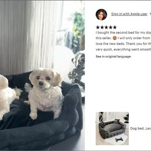 May include: Two small white dogs are resting on a large, dark gray dog bed. The bed has a plush, velvety texture and is surrounded by pillows. The dogs appear comfortable and relaxed. The image also includes a customer review.