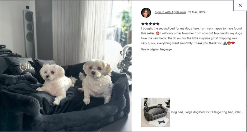 May include: Two small white dogs are resting on a large, dark gray dog bed. The bed has a plush, velvety texture and is surrounded by pillows. The dogs appear comfortable and relaxed. The image also includes a customer review.