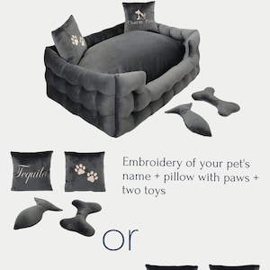 May include: A gray pet bed with a tufted design, accompanied by pillows and toys. The image shows options: embroidery of a pet's name, a pillow with paw prints, and two toys, or brand logo embroidery, a paw print pillow, and two toys.