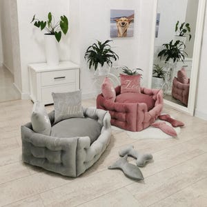 May include: Two plush dog beds in gray and pink, with matching pillows embroidered with names. The gray bed has the name "Luna" embroidered on the pillow. The pink bed has the name "Zoe" embroidered on the pillow. Additional dog toys are also visible.