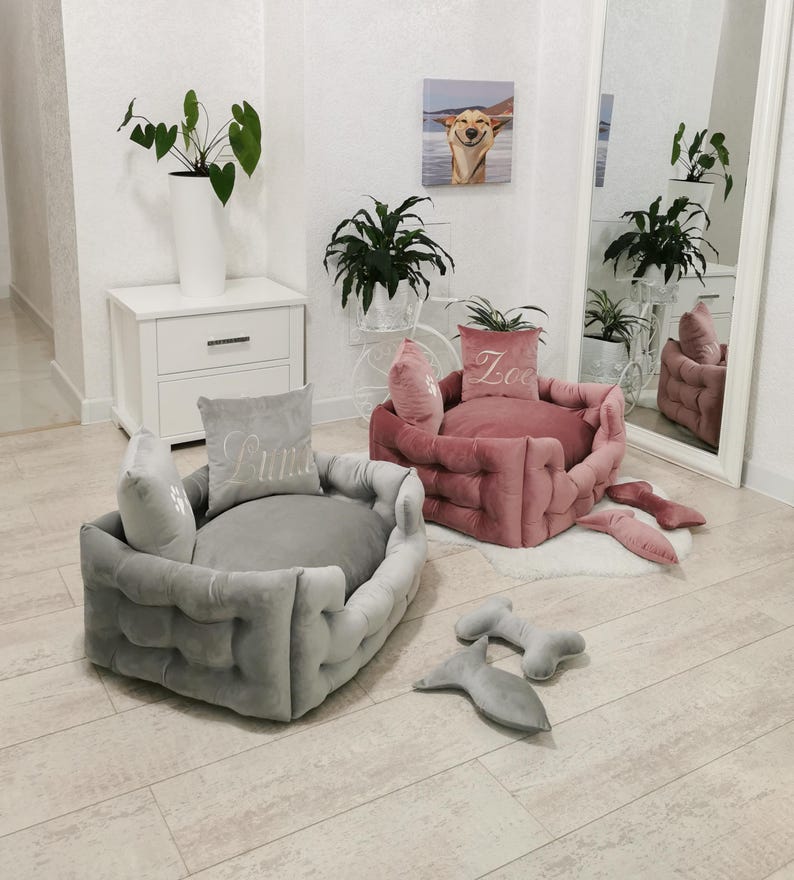 May include: Two plush dog beds in gray and pink, with matching pillows embroidered with names. The gray bed has the name "Luna" embroidered on the pillow. The pink bed has the name "Zoe" embroidered on the pillow. Additional dog toys are also visible.