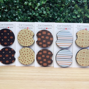 May include: Five sets of two circular car coasters on white display cards labeled Car Coasters Handmade with love. The designs include black pumpkin patterns, tan polka dots, brown pumpkin prints, horizontal stripes, and tan checkered pumpkin motifs.