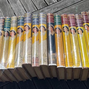 May include: A collection of vintage books with yellow spines, featuring portraits of a woman on the covers. The books are arranged in a row, with varying colors on the spines, including red, blue, and green.