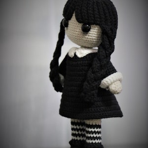 May include: A crocheted doll with black hair, a black dress, white collar, black and white striped stockings, and black shoes.