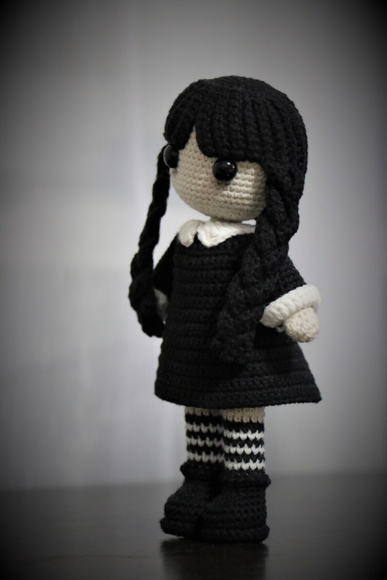 May include: A crocheted doll with black hair, a black dress, white collar, black and white striped stockings, and black shoes.