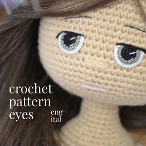 Peut inclure: Gros plan sur le visage d'une poupée en crochet avec des yeux gris et une perruque brun clair. Le texte "crochet pattern eyes eng ital" est visible sous le visage de la poupée.