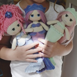 May include: Three crocheted mermaid dolls with pink, purple, and green tails. The dolls have pink yarn hair and are wearing crocheted tops.
