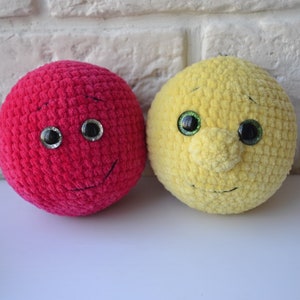 May include: Two crocheted plush toys with smiling faces. One is red and the other is yellow.