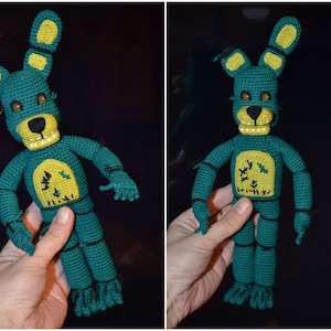 Może przedstawiać: Zielona i żółta pluszowa zabawka szydełkowa przypominająca królika z długimi uszami. Zabawka ma czarny nos, białe zęby i żółte oczy. Zabawka trzyma ramiona rozłożone na boki.