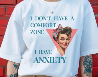 Może przedstawiać: Biała koszulka z nadrukiem graficznym kobiety z różową kokardką we włosach. Tekst na koszulce brzmi "I don't have a comfort zone I have anxiety".