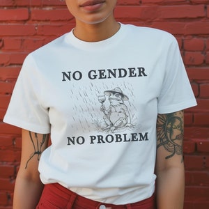 May include: White t-shirt featuring a black frog illustration holding a glass of wine. The text "NO GENDER NO PROBLEM" is printed on the shirt.