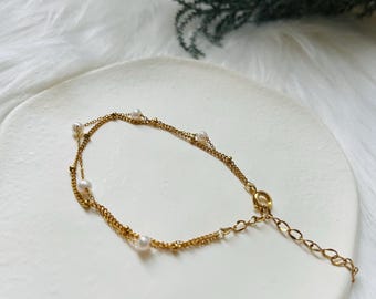 May include: A delicate gold chain bracelet with small white pearls. The bracelet has a lobster clasp closure.