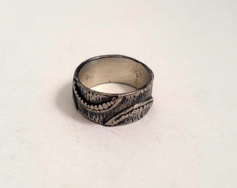 May include: A silver ring with a textured band and a design of curved lines and dots.