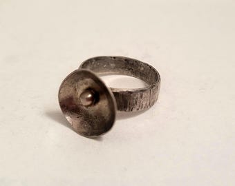 May include: A silver ring with a textured band and a round, disc-shaped top.