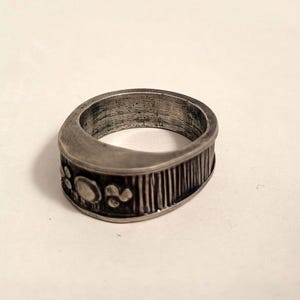 May include: A silver ring with a textured band and a design of small circles and dots.